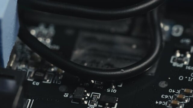 Macro slider shot of a disassembled UPS circuit board. Selective focus moving over blue thermal pad, wires, and various micro electronic components on PCB surface. High-tech engineering background.