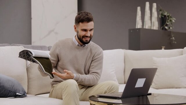 Man choosing fabric samples for home interior design sitting on sofa with laptop in furniture showroom