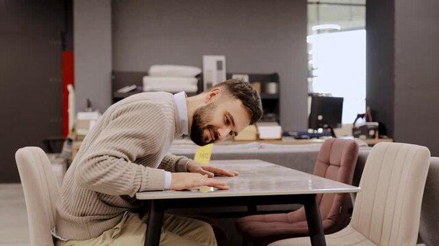 Man checking table quality in furniture store, carefully inspecting new furniture for purchase and home interior design