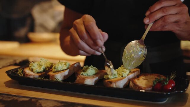 Close-up of a Chef Preparing Avocado Bruschetta on Toasted Bread with Cherry Tomatoes in a Restaurant Kitchen