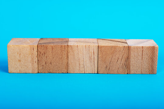 A row of five blank wooden cubes on a bright blue background. Minimalist concept for business strategy, building blocks, and step-by-step planning with copy space.