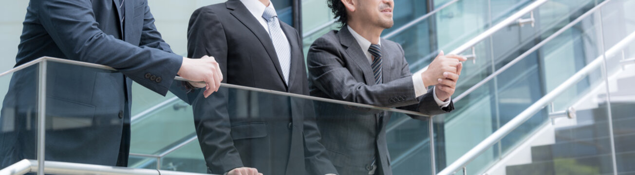 屋外のビル背景で未来を見据え笑顔で語る会社のビジネスマンチームの成長と挑戦　プロジェクトの成功などのポジティブ前向き上司、部下など3人チームのイメージバナー顔無し