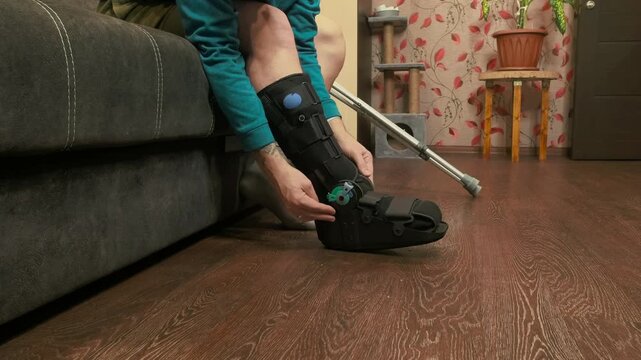Man adjusting medical boot on injured leg close up, rehabilitation process, orthopedic recovery and health care concept.