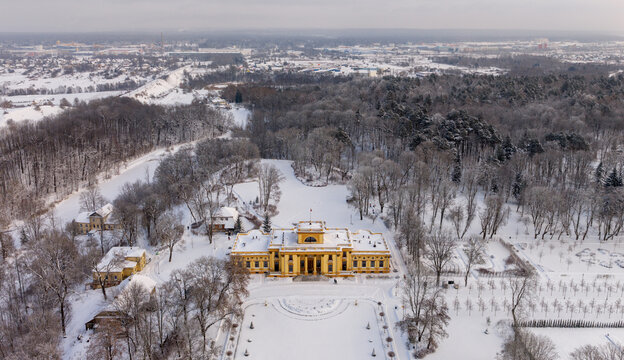 Aerial view of the yellow neoclassical Traku Voke Manor surrounded by snow-covered parkland and bare winter trees in Vilnius, Vilniaus apskritis, Lithuania.