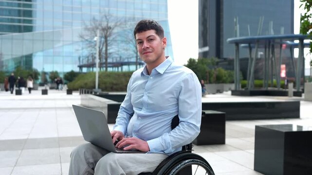 Young businessman with a physical disability sitting in a wheelchair while working on a laptop computer in a modern city financial district