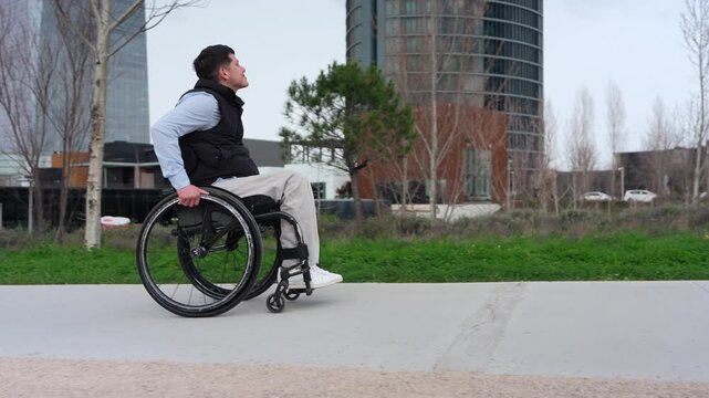 Young man with a disability confidently maneuvering his wheelchair along a sidewalk in a modern business district, showcasing resilience and mobility