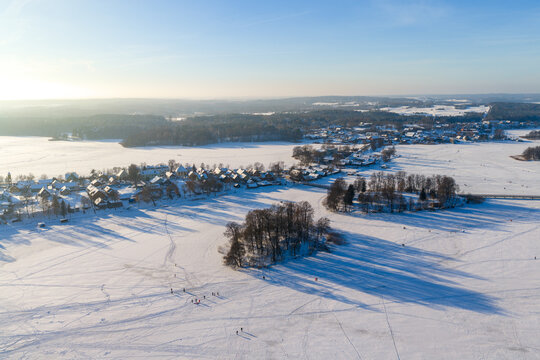 Aerial view of the snow-covered town and frozen Lake Galve with people walking on the ice under a clear blue sky Trakai, Vilniaus apskritis, Lithuania.