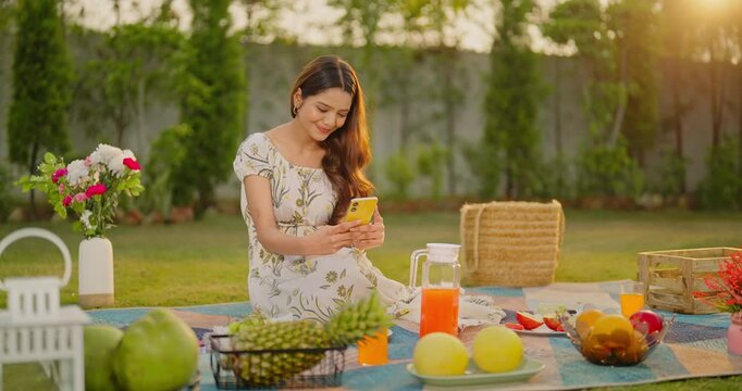 Indian young adult gen z female use mobile check phone look screen typing online do virtual chat enjoy picnic trip. Happy teen age girl female spend good break free time have fun joy at garden place