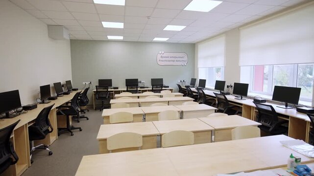 Modern IT classroom features computer workstations and rows of empty desks. Spacious room conveys bright functional learning environmen