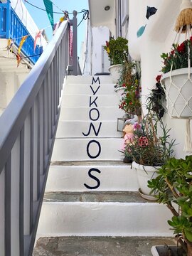 Photo of traditional whitewashed stone stairs with hand-painted 'Mykonos' lettering in a narrow alleyway of Chora, Mykonos island, Greece.