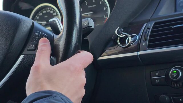 Man holding steering wheel inside modern car. Driver adjusting cruise control panel with thumb. Automobile interior transportation trip journey navigation technology.