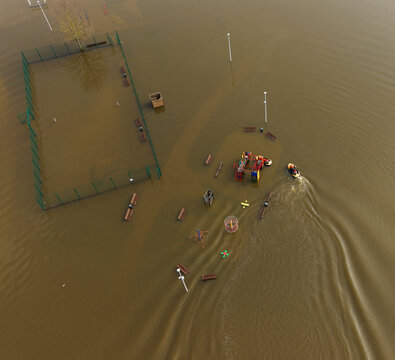 Aerial view of a flooded playground and sports court submerged under murky brown water with a small boat navigating through the area in Kedainiai, Kaunas County, Lithuania.