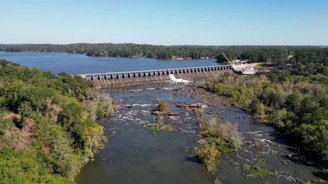 Oliver Dam on Chattahoochee River in Columbus Georgia shows spillway discharge and exposed bedrock shoals downstream with Lake Oliver reservoir upstream, static aerial shot