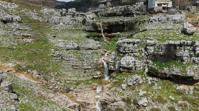 Aerial view of Qattin Azar waterfall flowing through layered rocky terrain in Baskinta, Lebanon, showing the natural beauty of the mountain landscape.