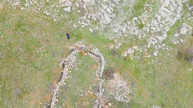 Overhead aerial clip of old World War II trench remains in Qattin Azar, Baskinta, surrounded by rugged stones, grass, and natural mountain terrain.