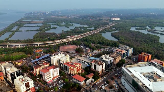 Cinematic aerial view of KTC Bus Stand surrounded by modern buildings, busy roads, and parking areas, with elevated highways stretching toward wetlands and distant landscapes.