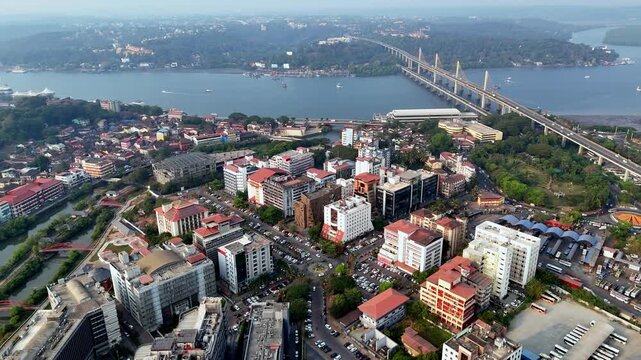 Cinematic aerial view of the entire Panaji city showcasing a vibrant cityscape with dense buildings, busy roads, and the Mandovi River flowing alongside, with Atal Setu stretching across the horizon.