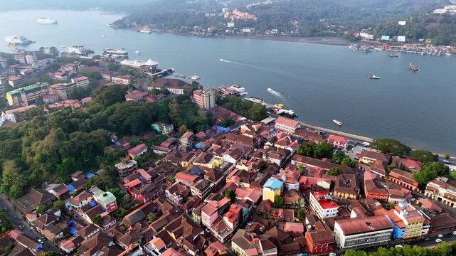 Wide cinematic aerial of the Mandovi River showcasing floating casino ships, passing boats, and a vibrant riverside skyline, blending leisure, movement, and scenic waterfront views. Sao Tome, Rua