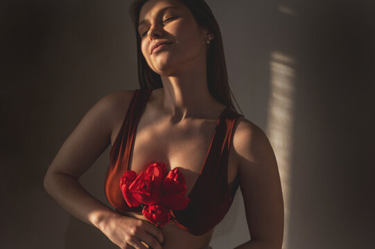 A blurry portrait of an attractive young woman holding a red tulip. A symbol of the female cycle, an allegory for menstruation and intimate health. A gynecological concept. woman breast cancer
