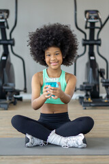 Naklejka premium A young child sit cross-legged on yoga mat, smiling while holding a blue drink, suggesting a focus on health and wellness indoors.