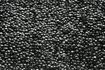 Fototapeta premium Glossy black polyethylene granules fill the frame as detailed texture for plastic manufacturing and recycling industry projects.