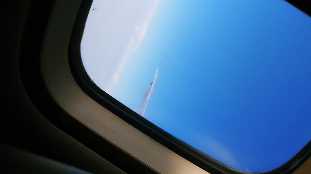 Airplane window view of blue sky with contrails