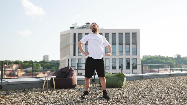 A man practices stretching exercises on a sunny rooftop overlooking a cityscape