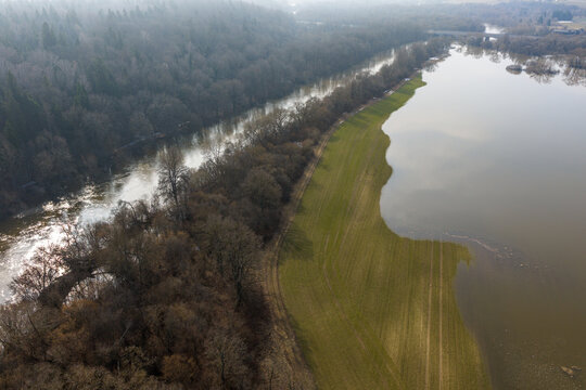 Aerial view of flooded green fields and a winding river bordered by a dense forest under a hazy sky in Kaniukai, Kaunas County, Lithuania.