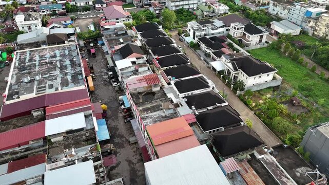 An aerial view showing a row of buildings and rooftops facing a narrow street, along with parked cars.