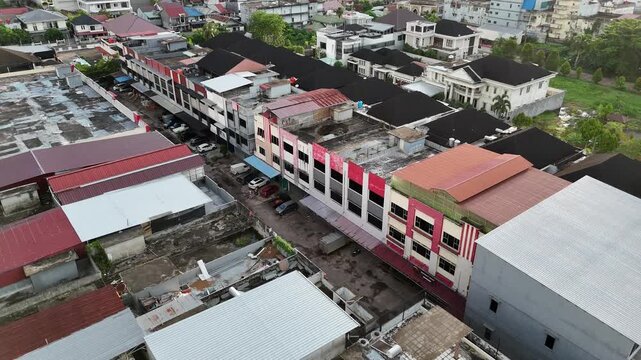 An aerial view showing a row of buildings and rooftops facing a narrow street, along with parked cars.
