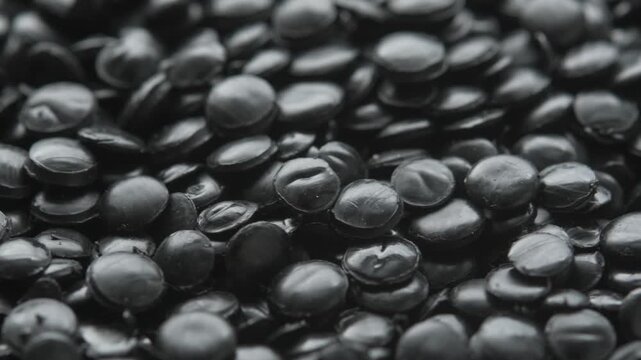 Close up of black polyethylene granules in slow rotation creates industrial plastic texture for recycling and production