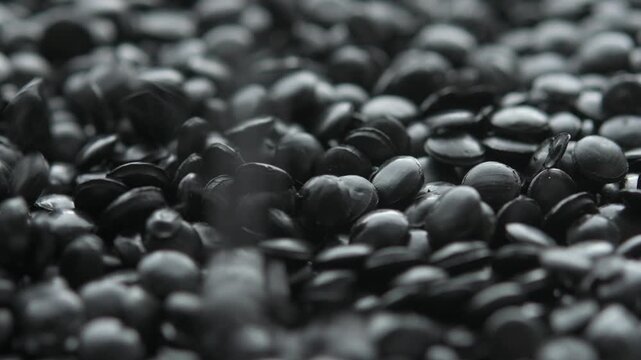 Black polyethylene pellets fall from above onto granules layer in macro, revealing raw polymer texture for industry use.