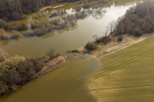 Aerial view of a flooded river overflowing into green agricultural fields with bare trees standing in murky water Kaniukai, Kaunas County, Lithuania.