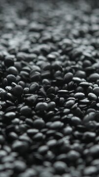 Black polyethylene granules fall from above into dark macro pile for plastic recycling and industrial material production