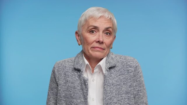 Clueless senior woman shrugging in confusion on blue