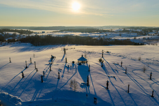 Aerial view of the Hill of Angels with wooden sculptures and a gazebo on a snow-covered field under a bright winter sun in Traku rajonas, Vilniaus apskritis, Lithuania.