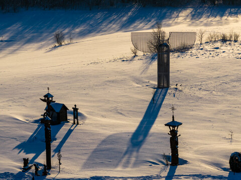 Aerial view of the Hill of Angels featuring wooden sculptures and a large metal angel casting long shadows on a snow-covered field in Traku rajonas, Vilniaus apskritis, Lithuania.