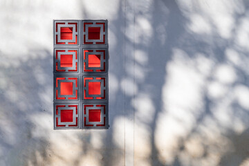 Exterior view of oriental grey and red Chinese style windows on white wall of resident building. The sunlight shines through trees and causes shadows on Chinese style house. © Surachetsh