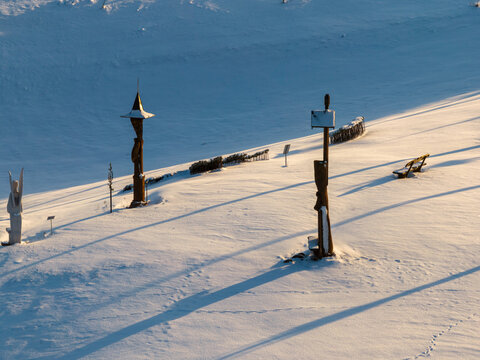 Aerial view of Hill of Angels with wooden sculptures casting long shadows over the pristine snow-covered landscape in Traku rajonas, Vilniaus apskritis, Lithuania.
