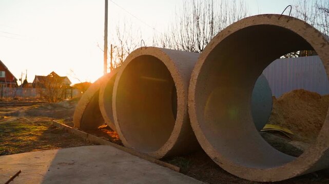 Concrete well rings for septic tank installation at golden hour sunset. Stacked precast concrete rings on construction site with sun flare
