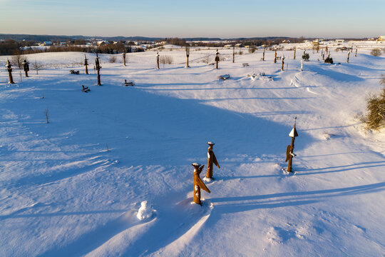 Aerial view of the Hill of Angels featuring wooden sculptures scattered across a snow-covered landscape under a clear winter sky in Traku rajonas, Vilniaus apskritis, Lithuania.