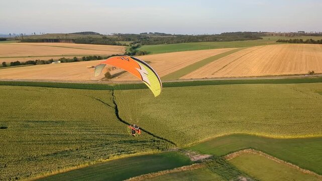 Aerial panorama of paragliding pilot with paramotor flying midair above landscape