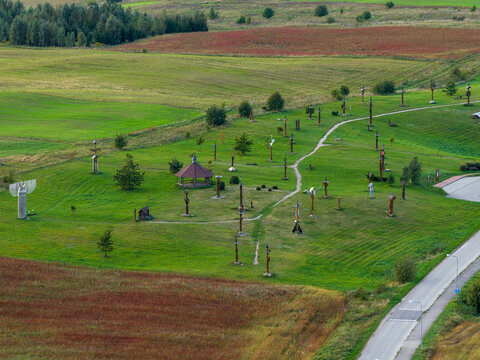Aerial view of the Hill of Angels featuring wooden sculptures and a gazebo among green meadows and colorful fields in Traku rajonas, Vilniaus apskritis, Lithuania.
