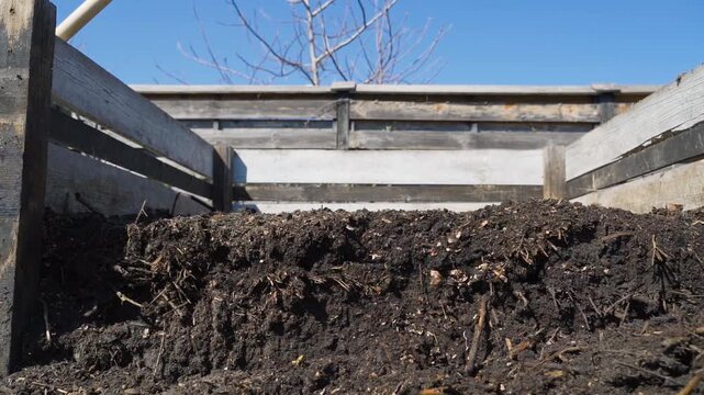 Compost pile in wooden bin in backyard garden during early spring. Organic decomposing matter with twigs and leaves in rustic compost bin