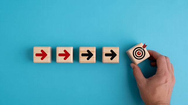 A hand places the final wooden block with a target and arrow symbol, completing a row of four blocks marked with red arrows pointing forward.