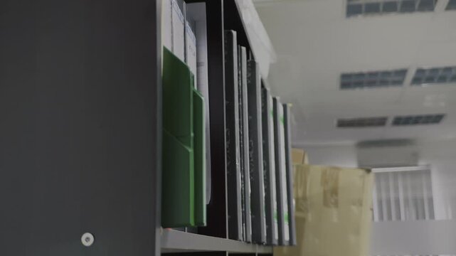Hand picking up a file or binder from a shelf, reviewing documents, and returning it to maintain organized business company records.