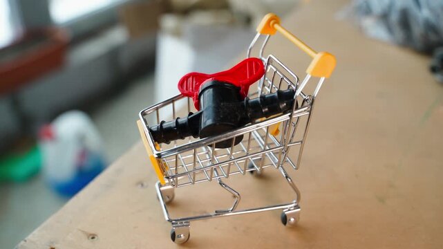 Hand placing plumbing valve into miniature shopping cart. Buying plumbing parts concept with small grocery cart and water valve