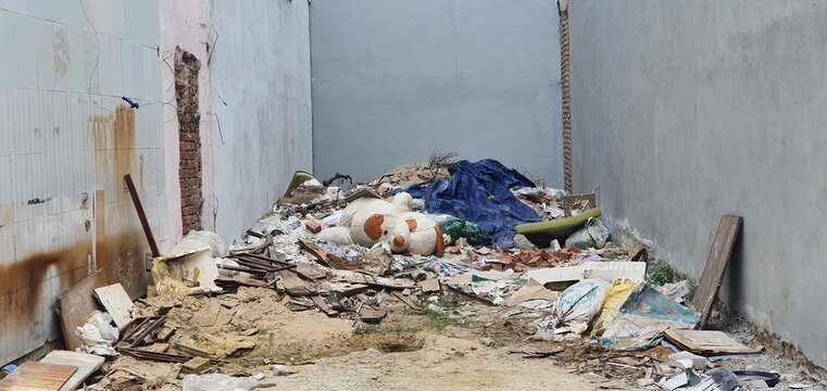 Abandoned dirty teddy bear dog lying on a large construction debris pile inside an alleyway between concrete walls, concepts of loss and displacement