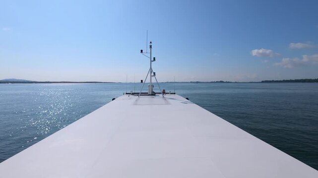 A smooth 60fps slow-motion 16:9 view from a ship's bow, highlighting the cinematic sun reflection on the sea and the steady progress of the vessel along the coast.