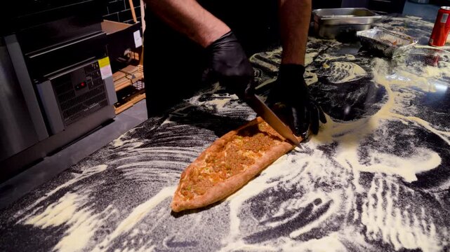 Man cutting Kasarli sucuklu pide and kiymali pide on the table in the bakery. Traditional Turkish flatbreads with meat and cheese toppings.